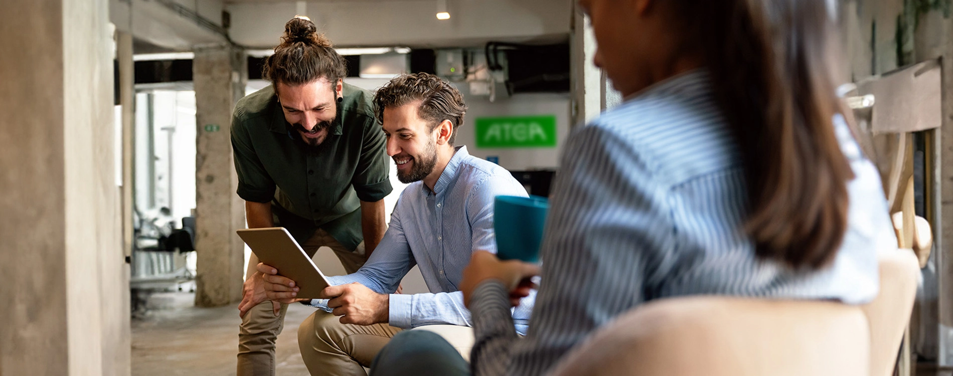 People sitting together in an office lounge, discussing work and using a tablet.