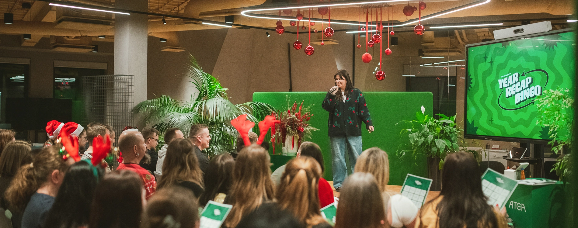 Employees attending an event and presentation in a modern office space, with a speaker presenting to an audience in front of a large display screen.
